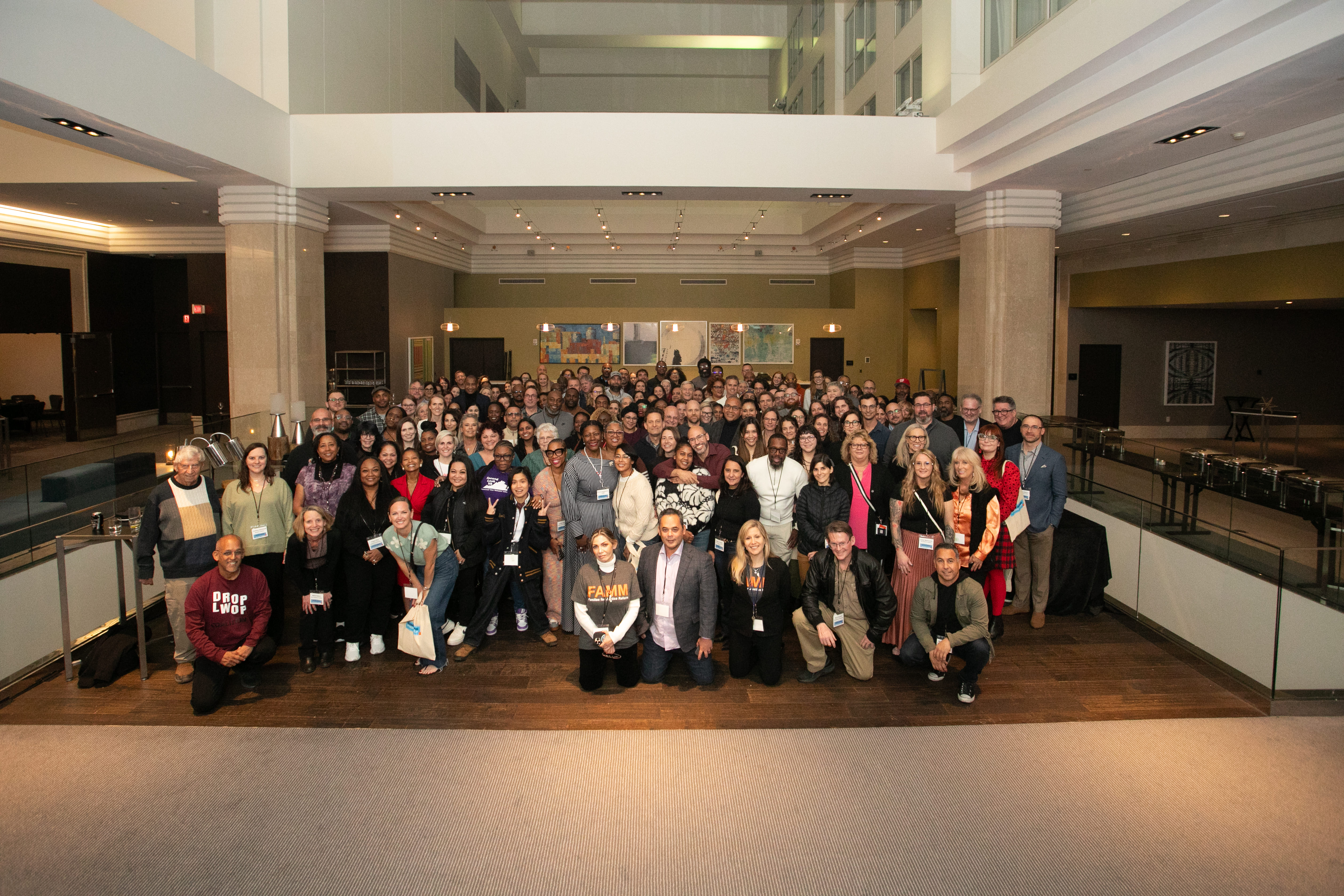 Large group photo of conference attendees gathered in a lobby space during an event.