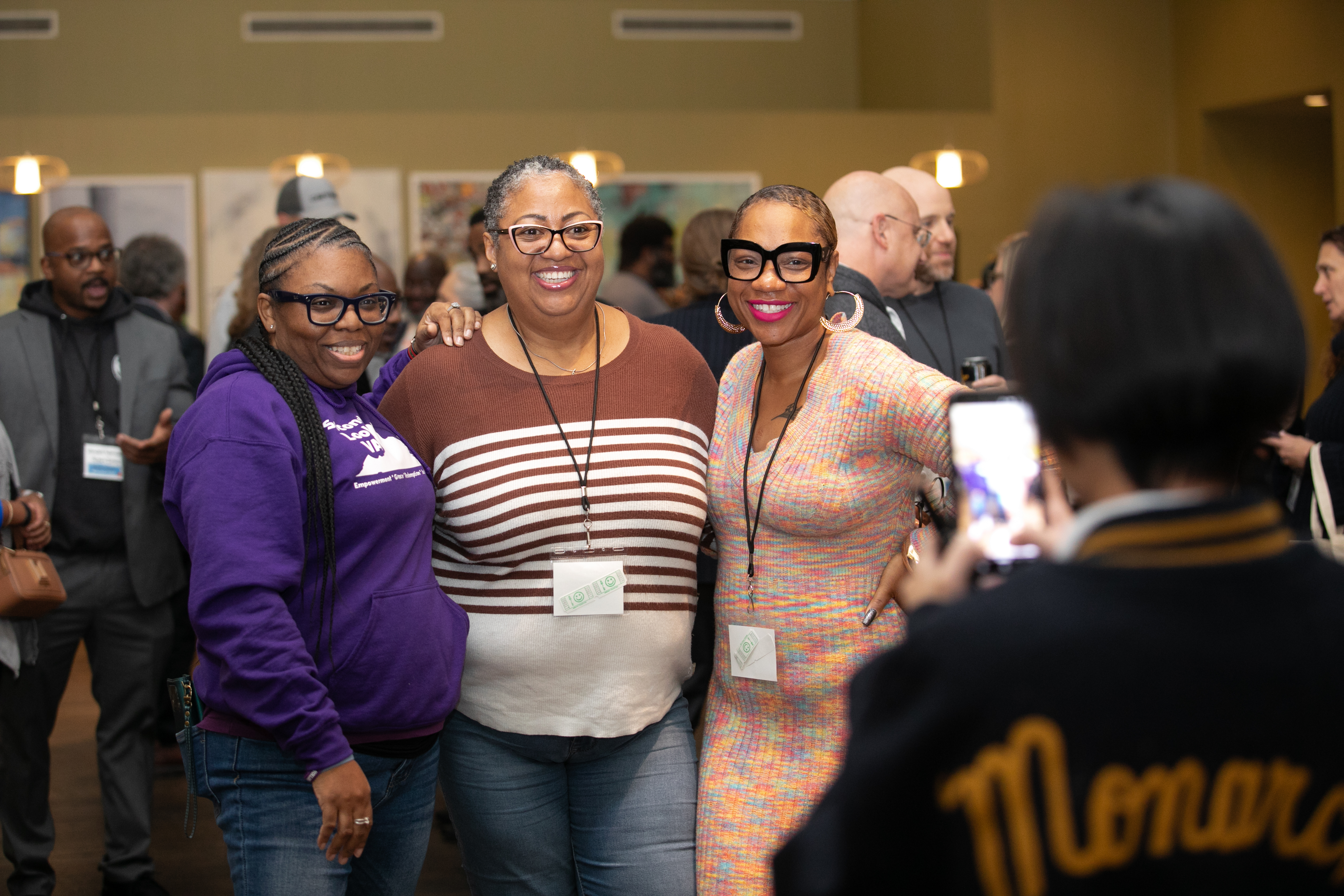 Three people posing together and smiling while someone takes their photo at a conference gathering.